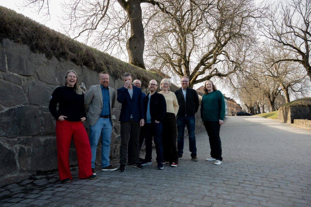 En gruppe mennesker står foran en murvegg og smiler.